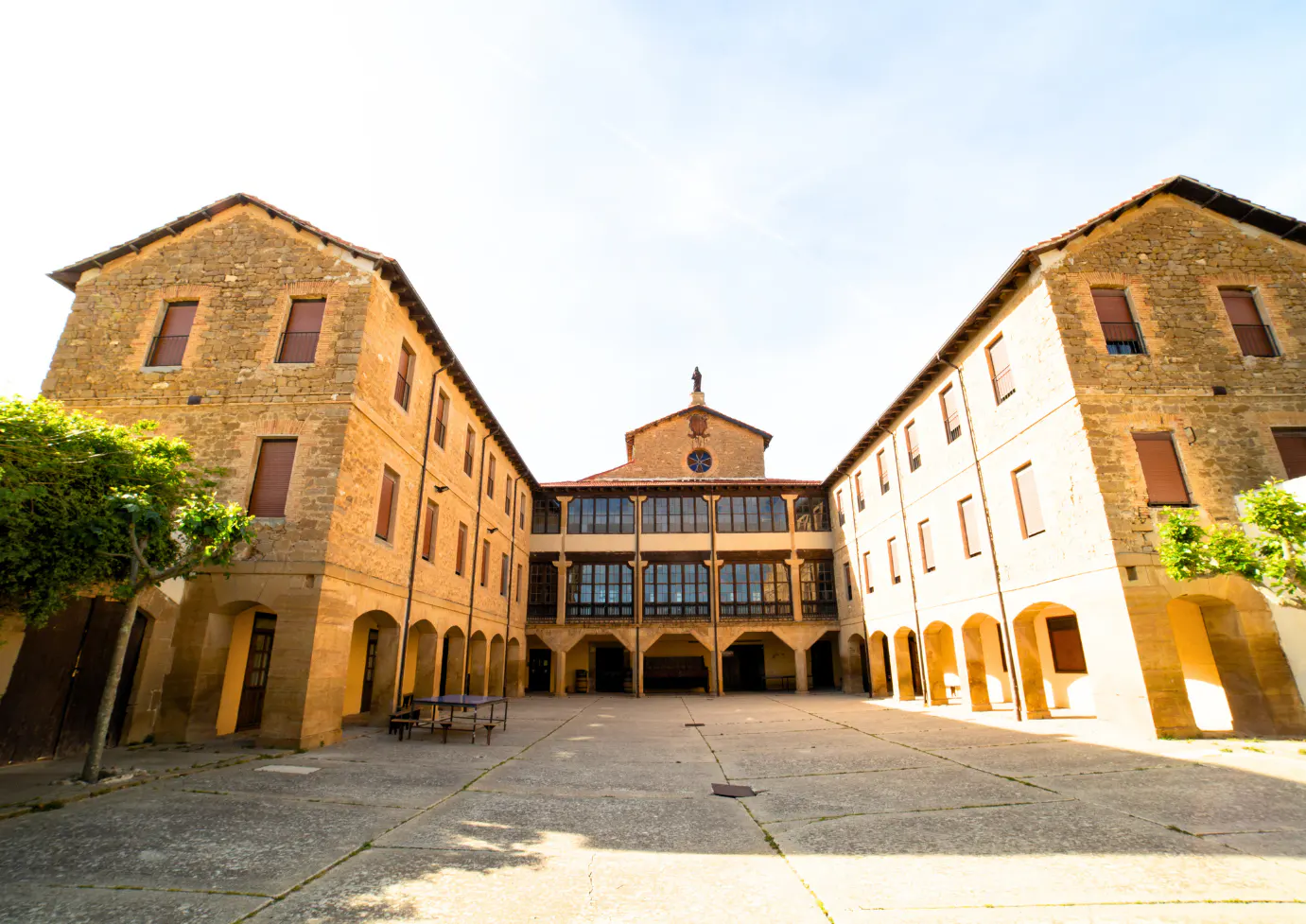 Courtyard view of a three-story, tan stone building with arched walkways and a statue on the roof.