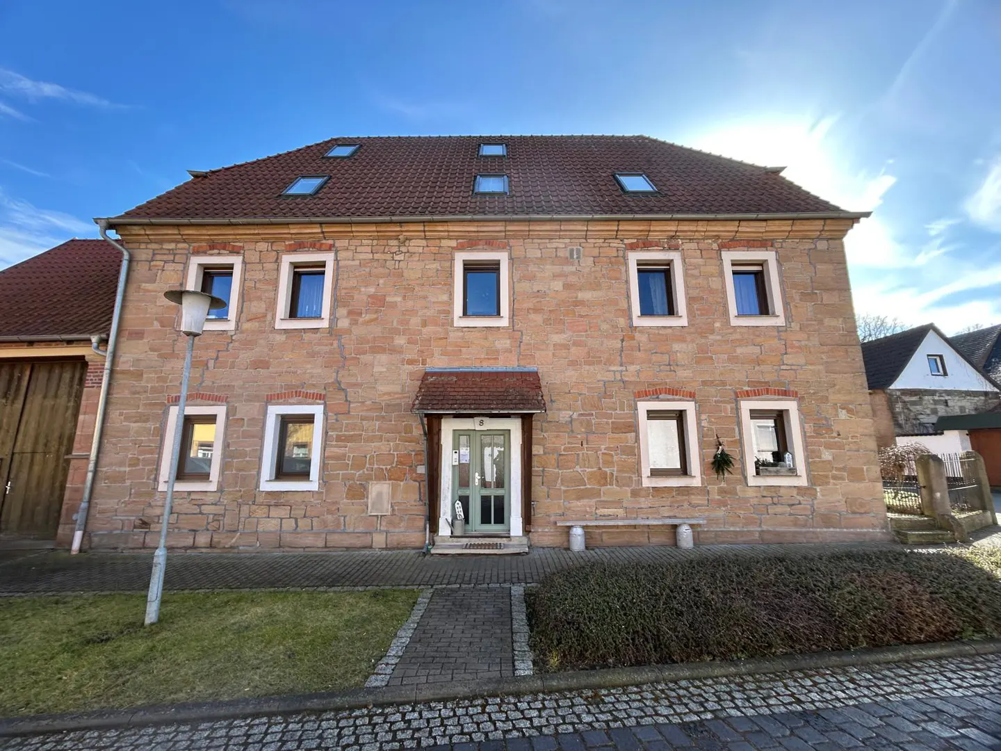 Two-story stone house with a red tile roof and green door under a sunny blue sky.