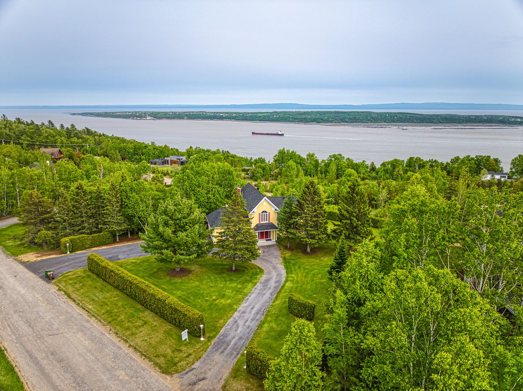 Aerial view of a yellow house with a red door, surrounded by lush green trees, a long driveway, and a view of the river. [AI-generated text]