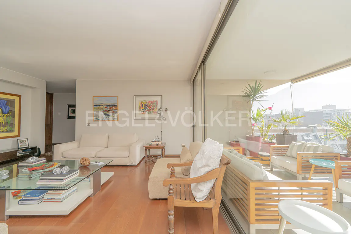 Bright living room with wood floors, white sofas, glass coffee table, and balcony with outdoor seating and plants.