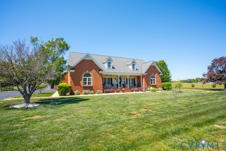 Brick house with a gray roof, white trim, and a front porch, surrounded by a green lawn and trees under a blue sky.