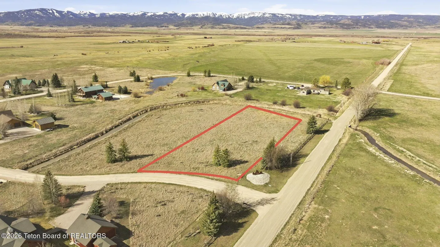 Aerial view of a vacant lot outlined in red, with mountains in the background. Houses and roads surround the property.