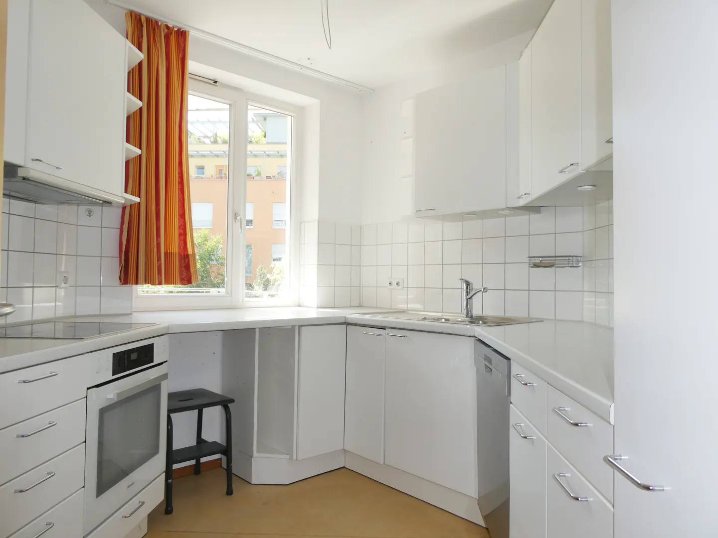 Bright kitchen with white cabinets, tiled backsplash, built-in oven, and a window with orange and yellow striped curtains.