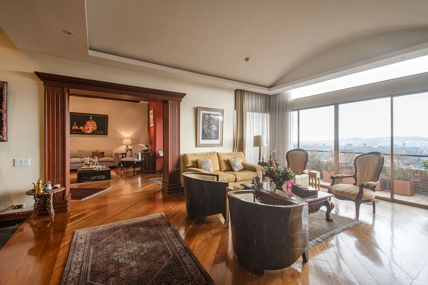 A luxurious living room with hardwood floors, a yellow sofa, and large windows overlooking a city.