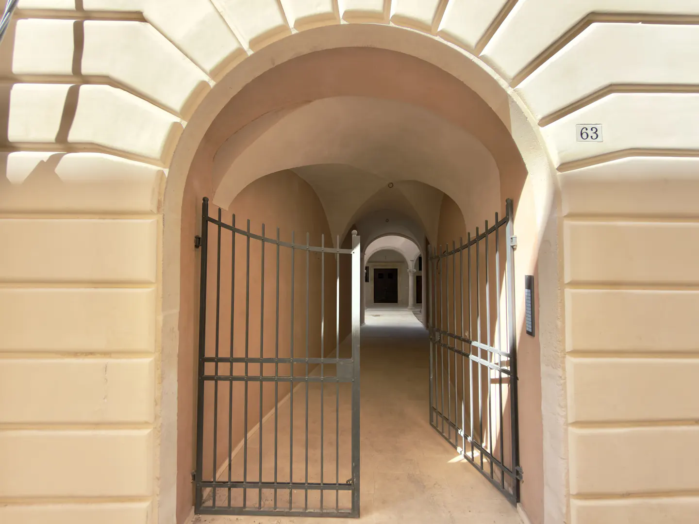 Arched entrance with open metal gate leading to a hallway with arched ceilings. Number 63 on the wall.