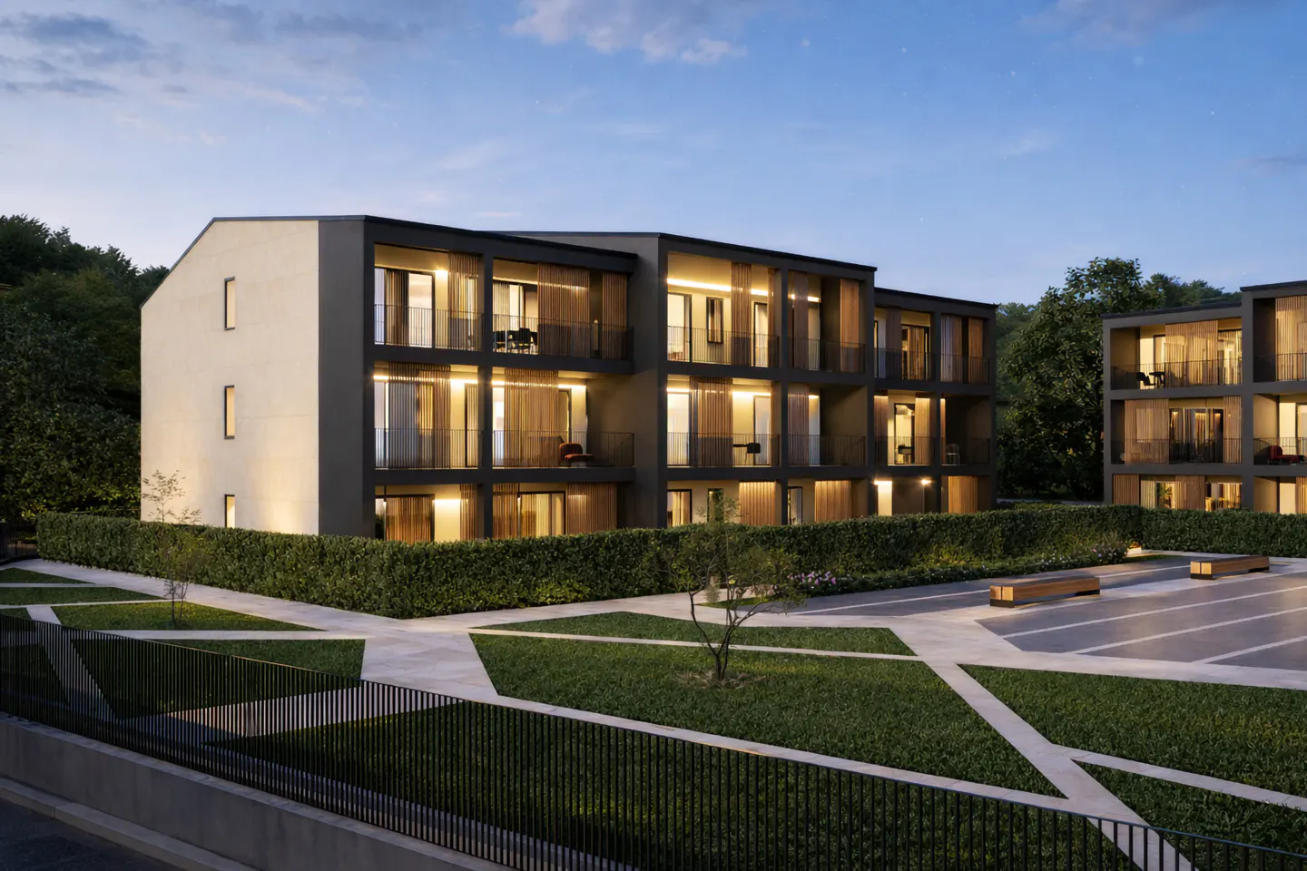 Modern apartment building with balconies at dusk. Green lawn and hedges surround the property. Warm light shines from the windows.
