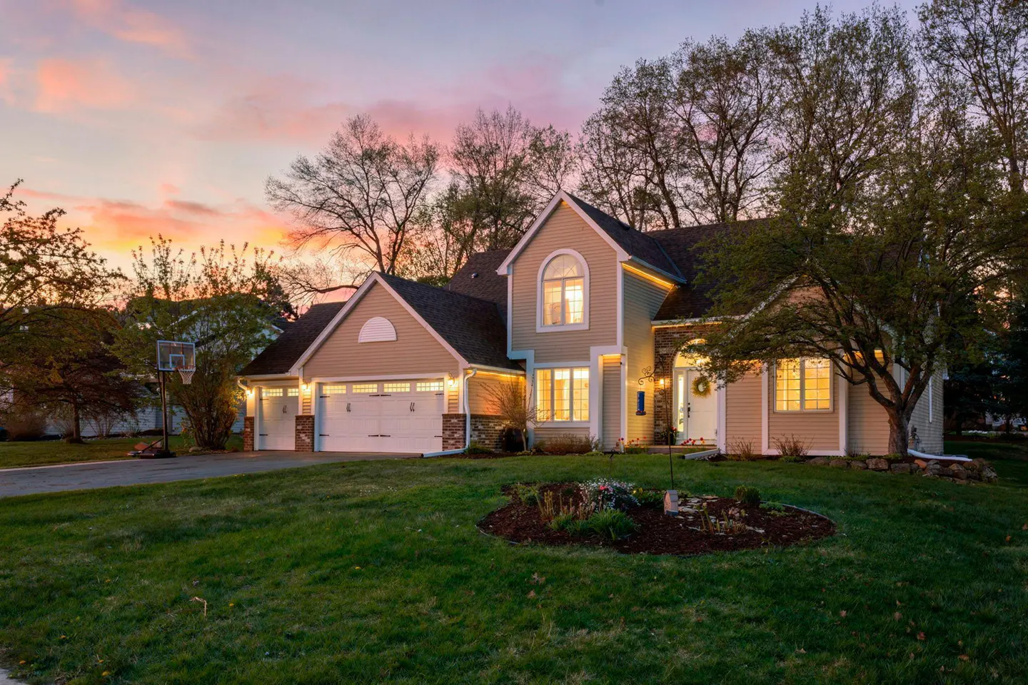 Beige two-story house with a three-car garage and a green lawn at sunset.
