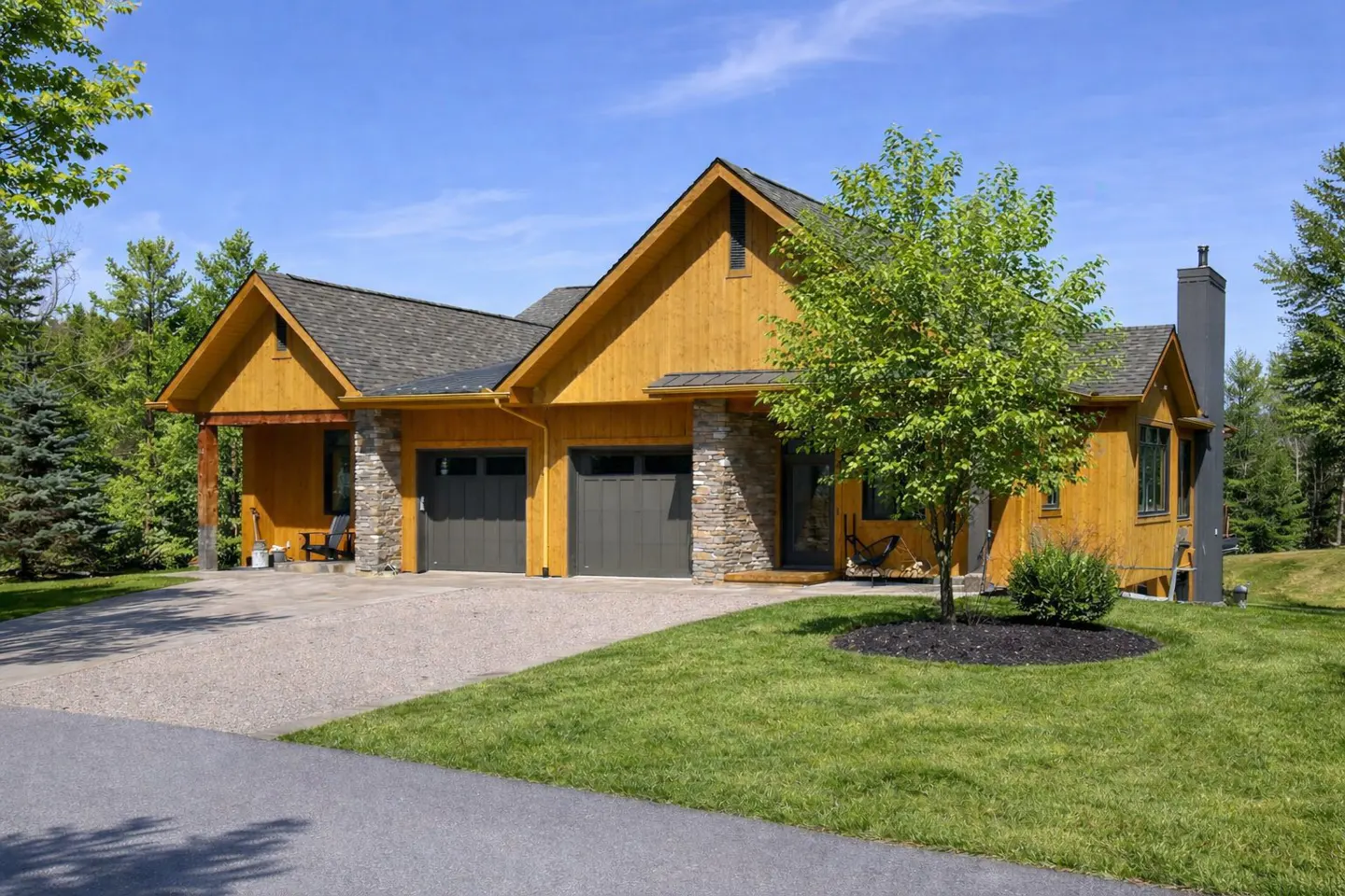 Exterior of a yellow house with a gray roof, stone accents, and a two-car garage. A green lawn and trees surround the house.