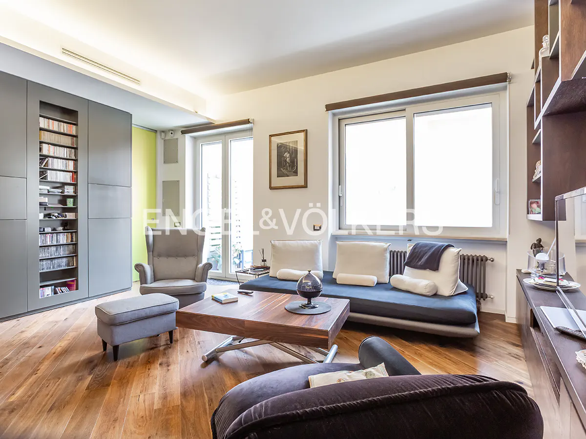 Living room with hardwood floors, gray built-in shelves, a blue sofa with white pillows, and a wooden coffee table. Natural light from windows.