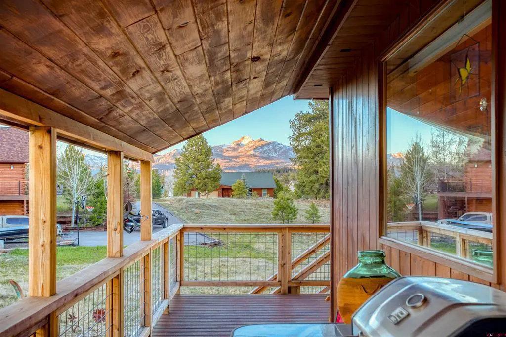 View from a wooden porch with a grill, looking out to a mountain view and a green lawn.