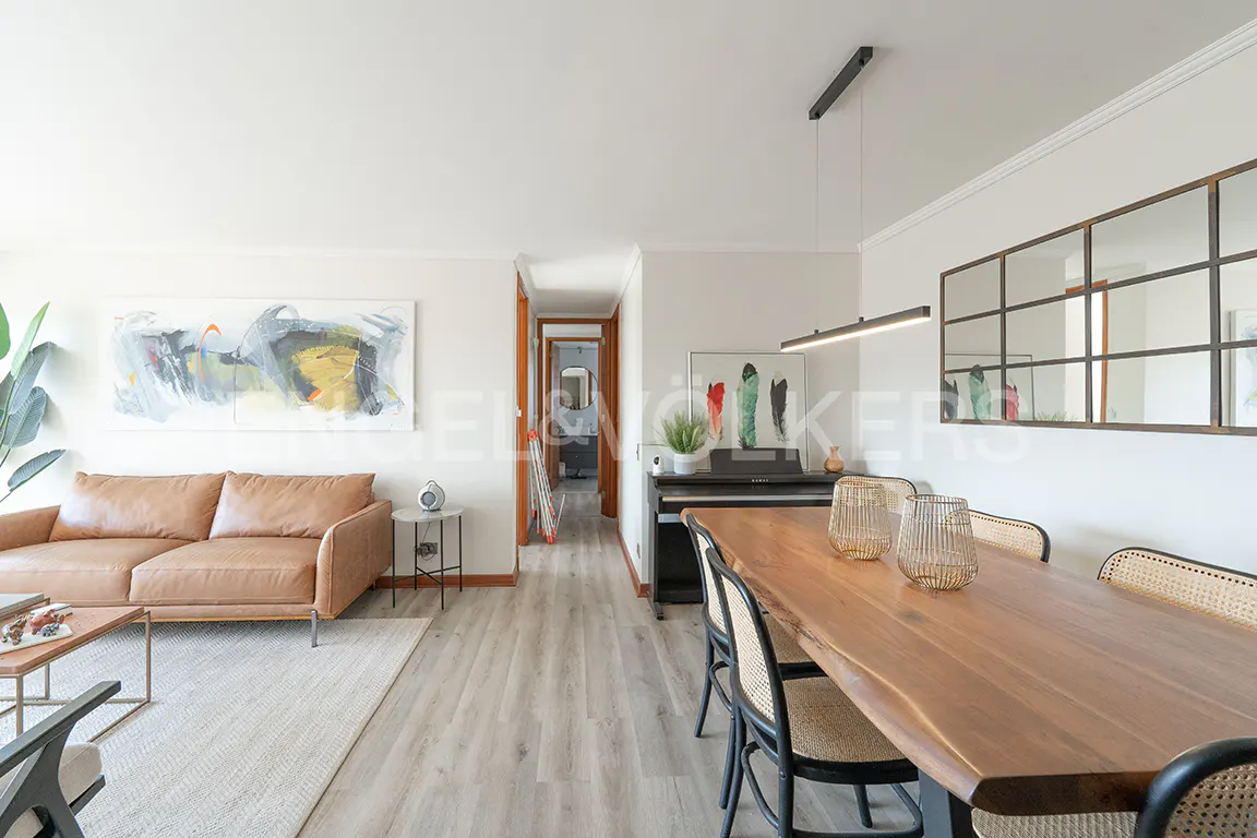 Bright living room with a brown leather sofa, wood dining table, piano, and abstract art on the walls.