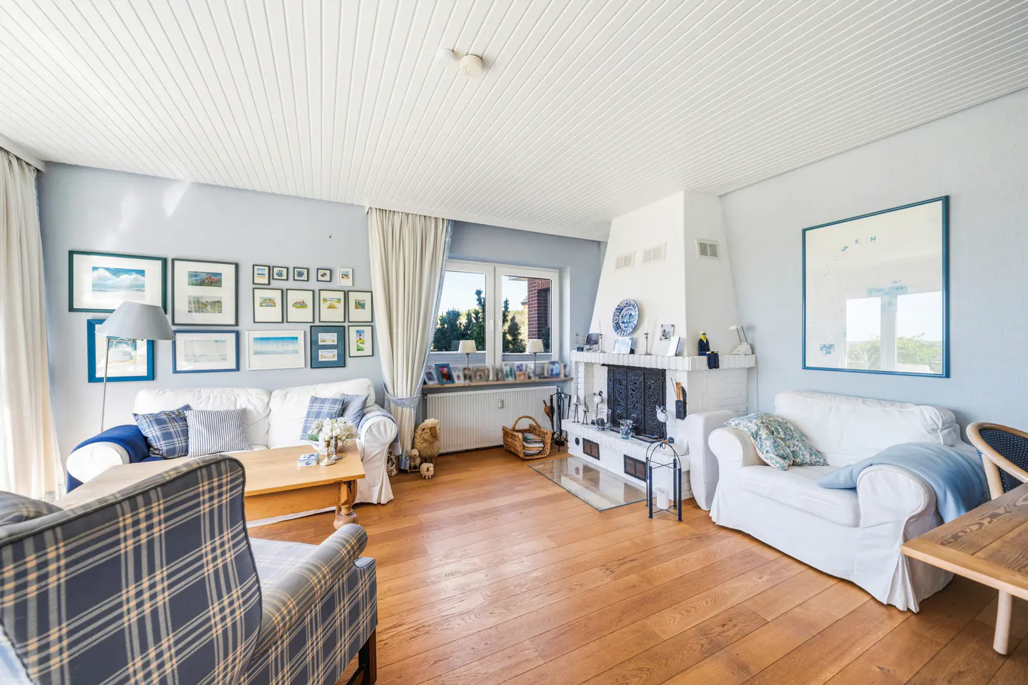 Living room with hardwood floors, white sofas, and a white fireplace. Blue and white accents, with framed art on the light blue walls.