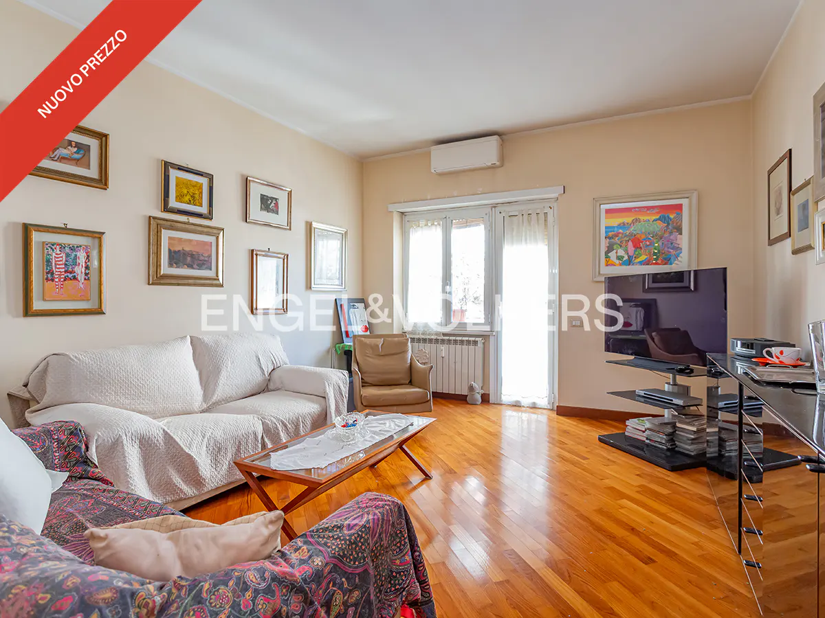 Bright living room with hardwood floors, sofas, a TV, and framed art on the walls. "Nuovo Prezzo" banner in the upper left corner.