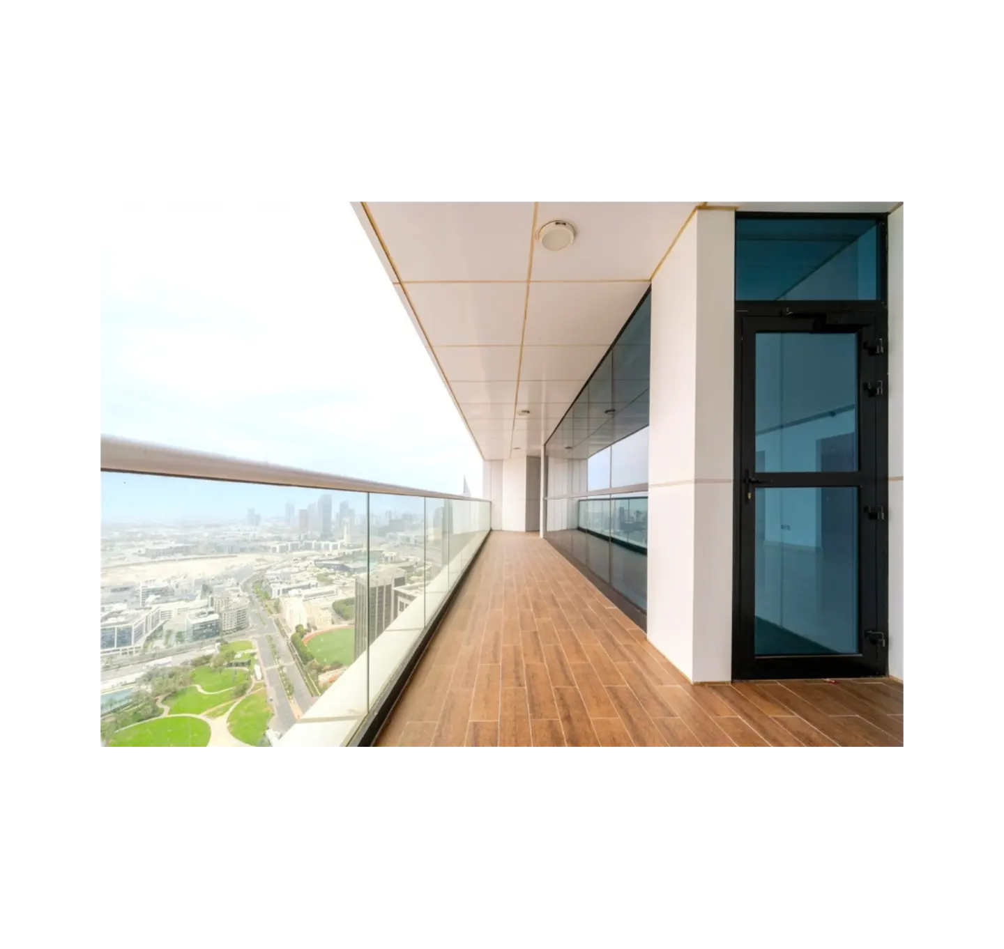 A long balcony with wood floors, glass railings, and a city view. A black door is on the right.