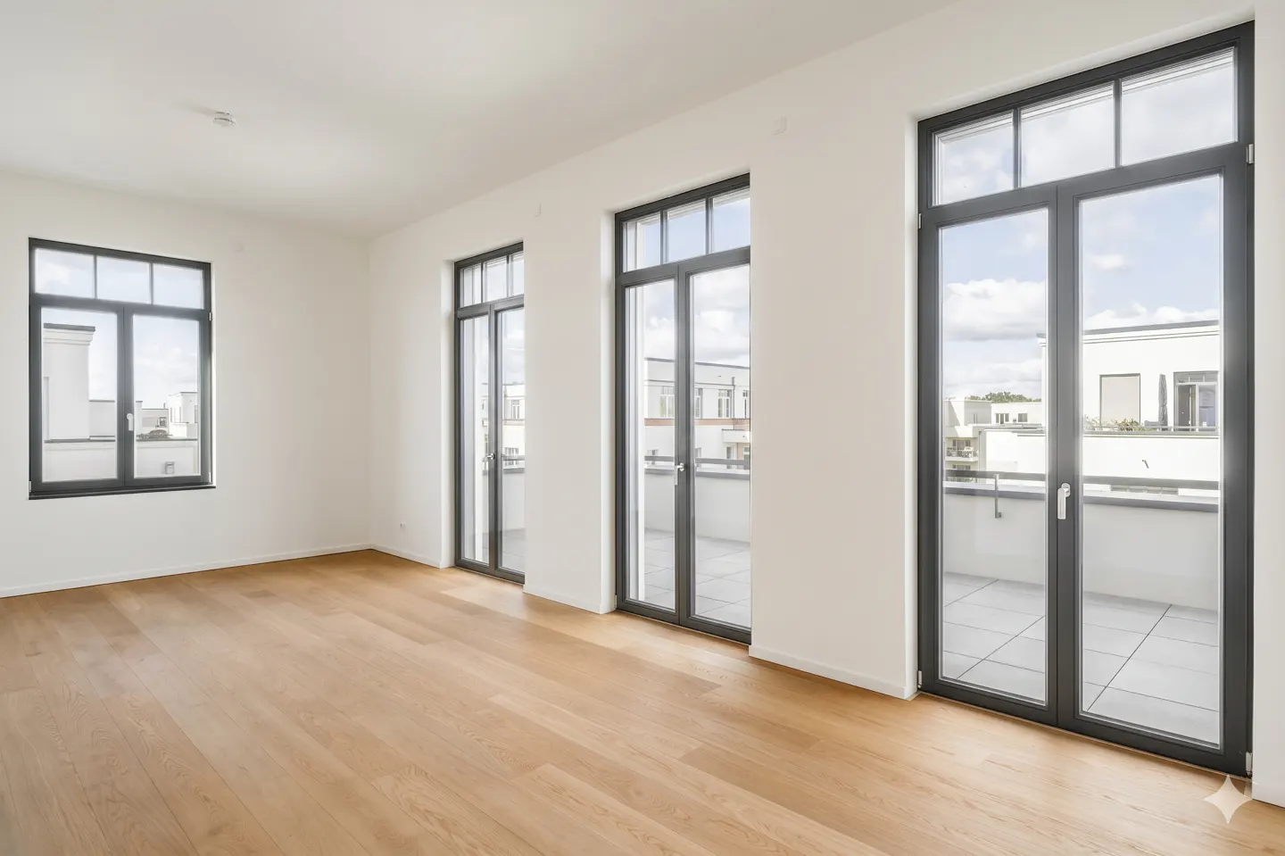 Bright, empty room with light wood floors, white walls, and black-framed windows and doors leading to balconies.
