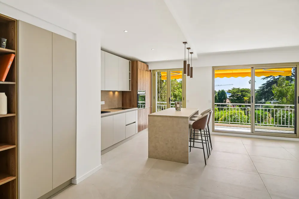 Bright, modern kitchen with white cabinets, island with stools, and balcony with yellow awning overlooking lush greenery.