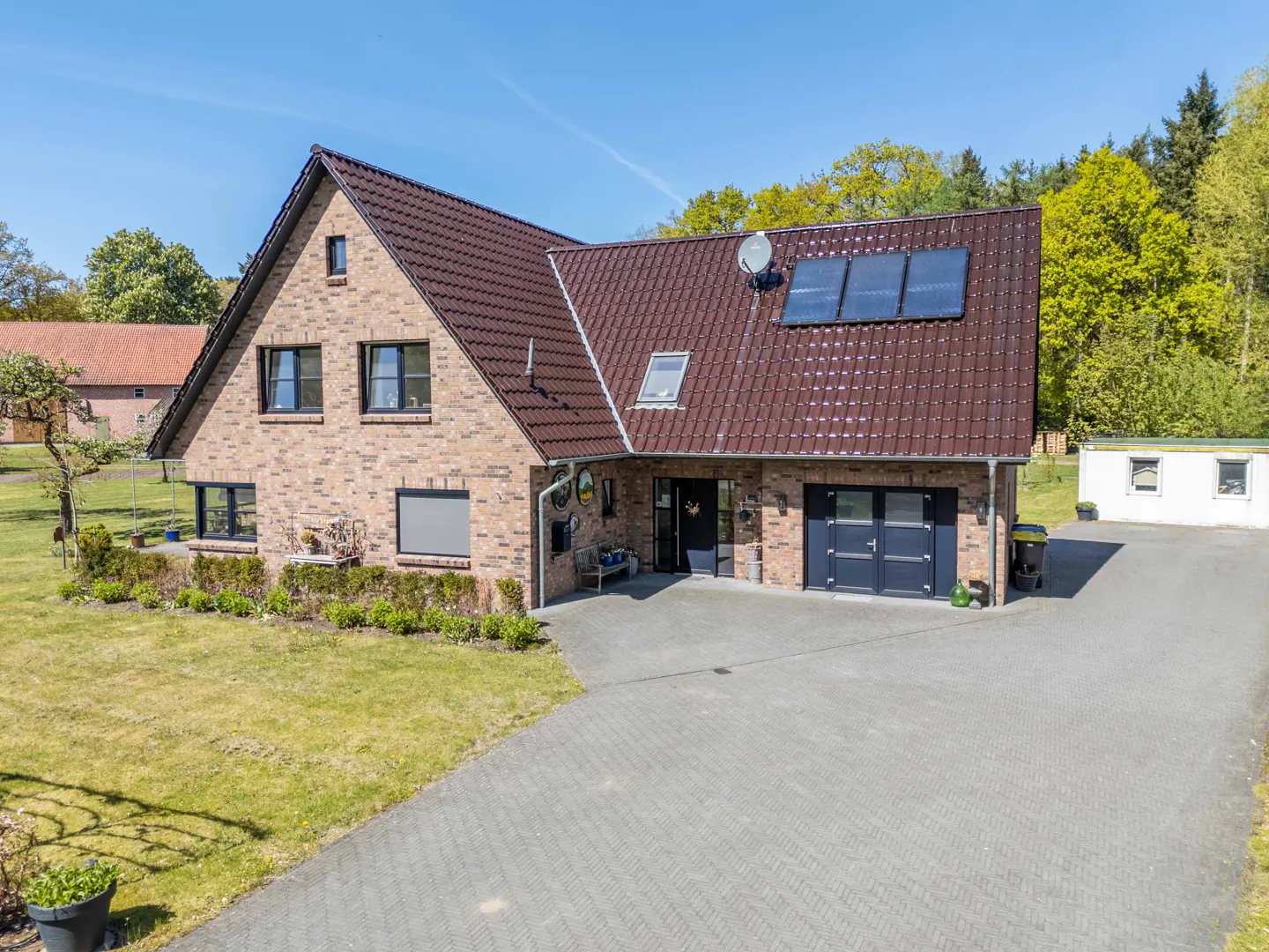 Two-story brick house with a brown roof, solar panels, and a gray driveway on a sunny day.