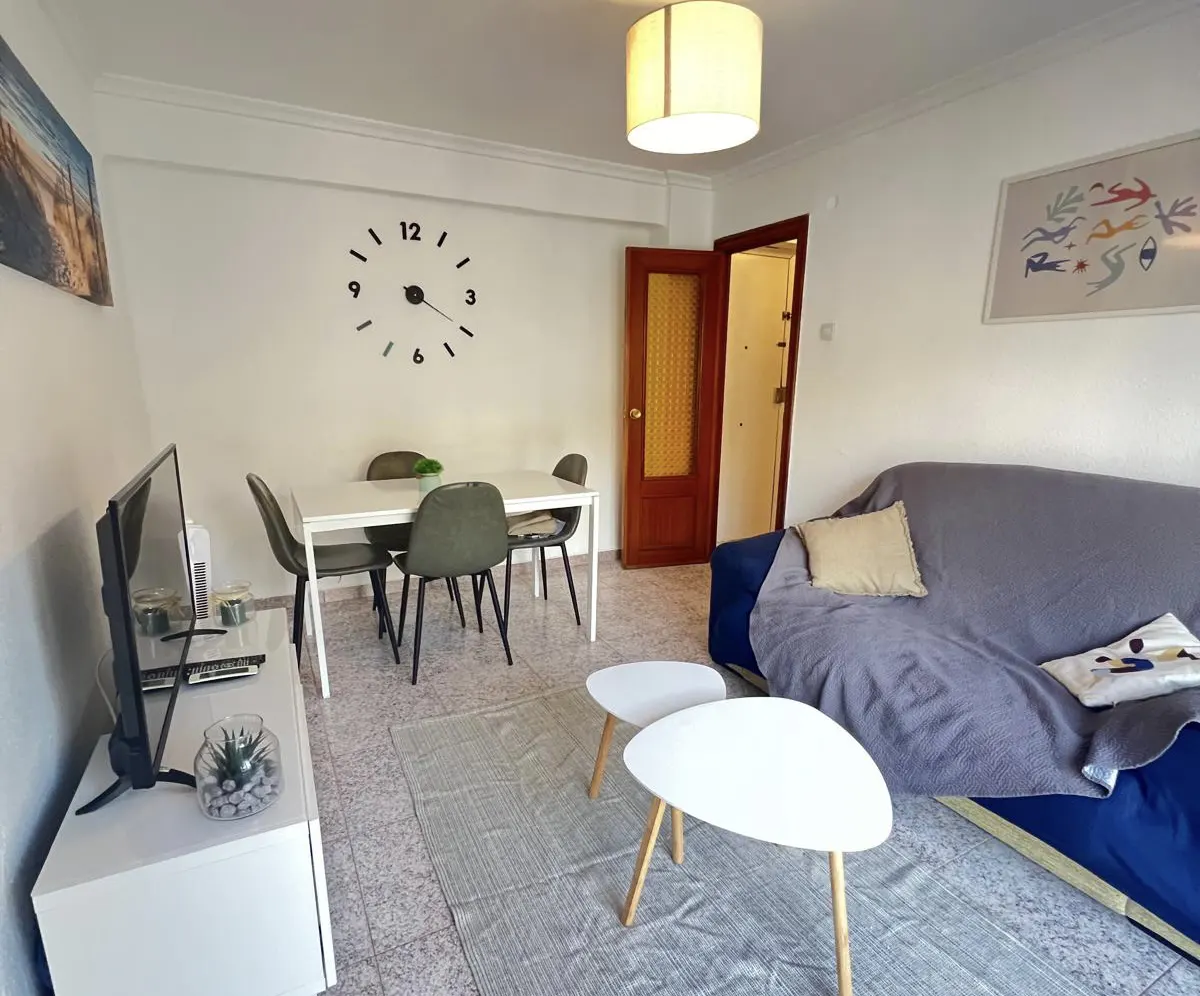 Living room with a blue sofa, two white coffee tables, a dining set with four chairs, and a large wall clock.