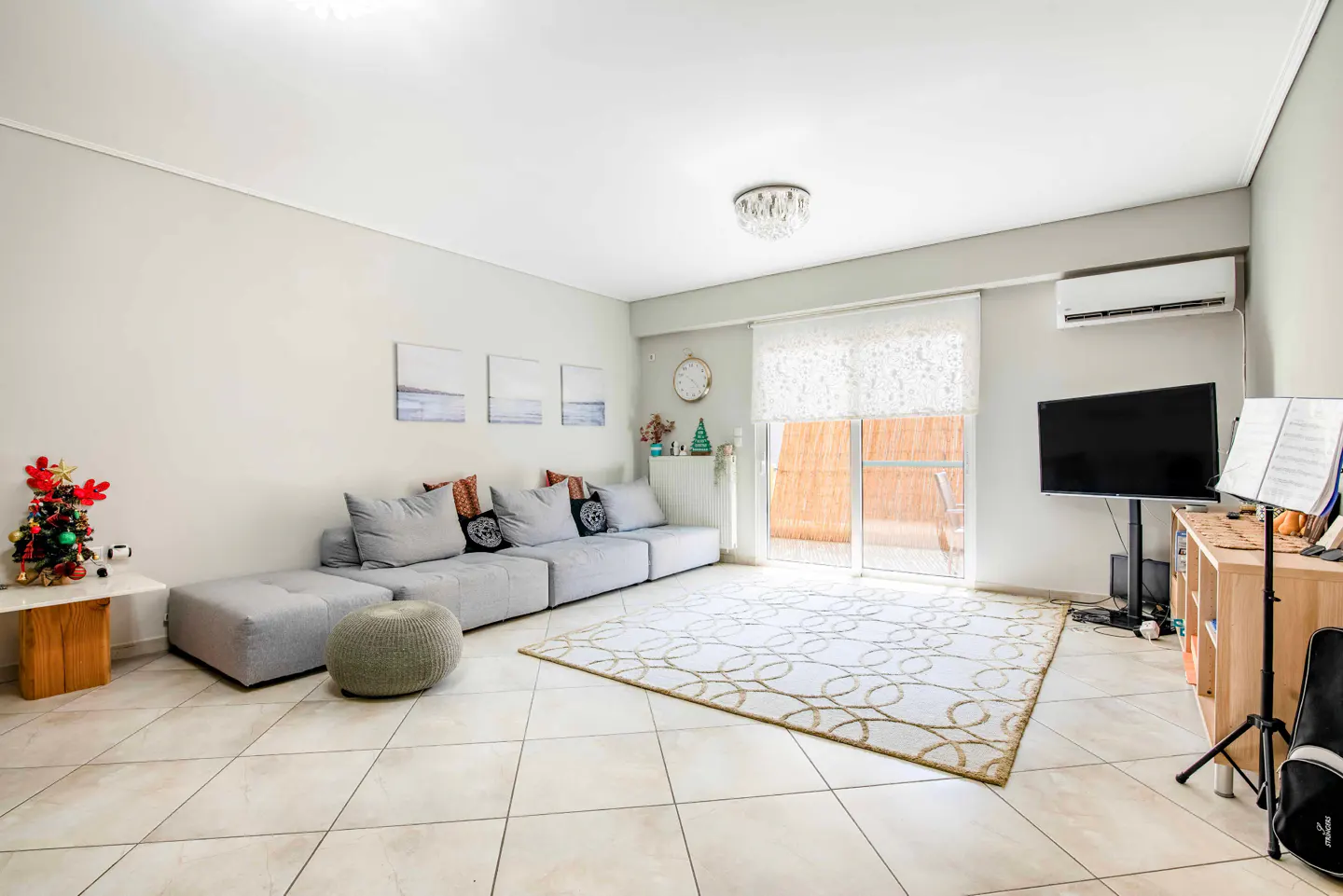Bright living room with a large grey sectional sofa, patterned area rug, television, and sliding glass doors to a balcony.