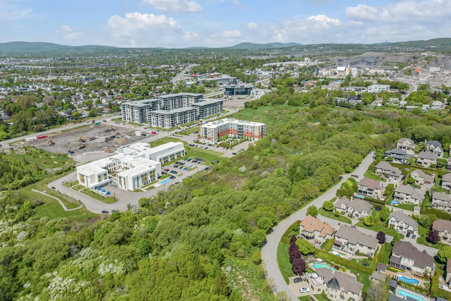 Aerial view of a suburban neighborhood with apartment complexes, residential homes, and green trees under a blue sky.