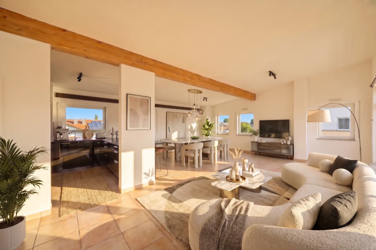 Bright, open-concept living space with white walls, wood beams, and tile floors. A cream sofa faces a TV, with a dining area and kitchen visible in the background.
