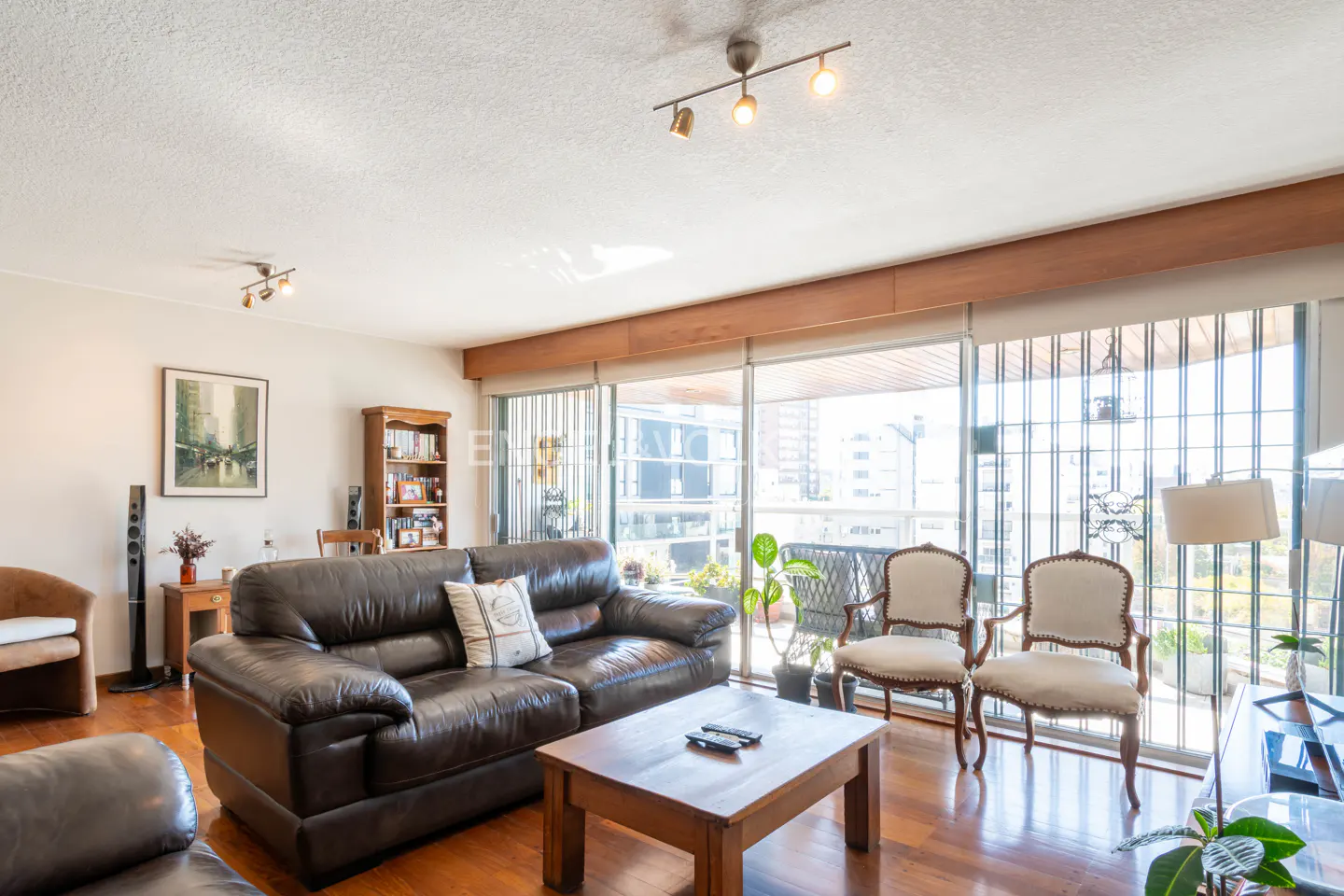 Bright living room with a brown leather sofa, wood coffee table, and two white chairs facing a large window.