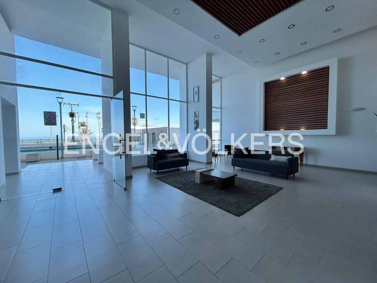 Bright lobby with ocean view features sofas, a rug, and tile floors. Engel & Völkers logo is visible.