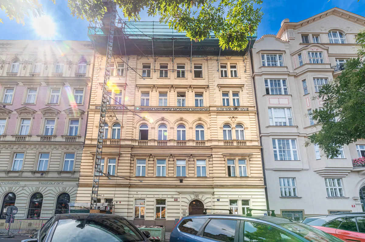 Street view of three buildings with scaffolding on the middle one. Cars are parked in front.