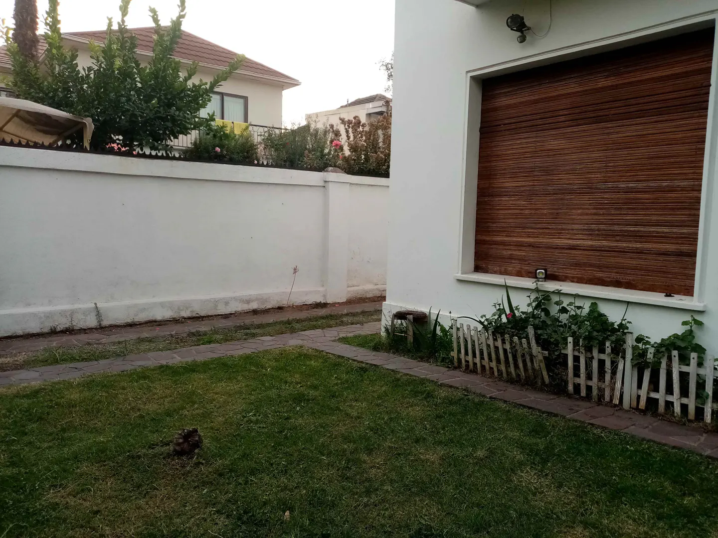 A white house with a brown window shutter, green lawn, and a white fence.