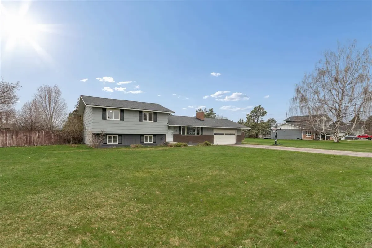 Two-story gray house with black shutters and a large green lawn under a blue sky.