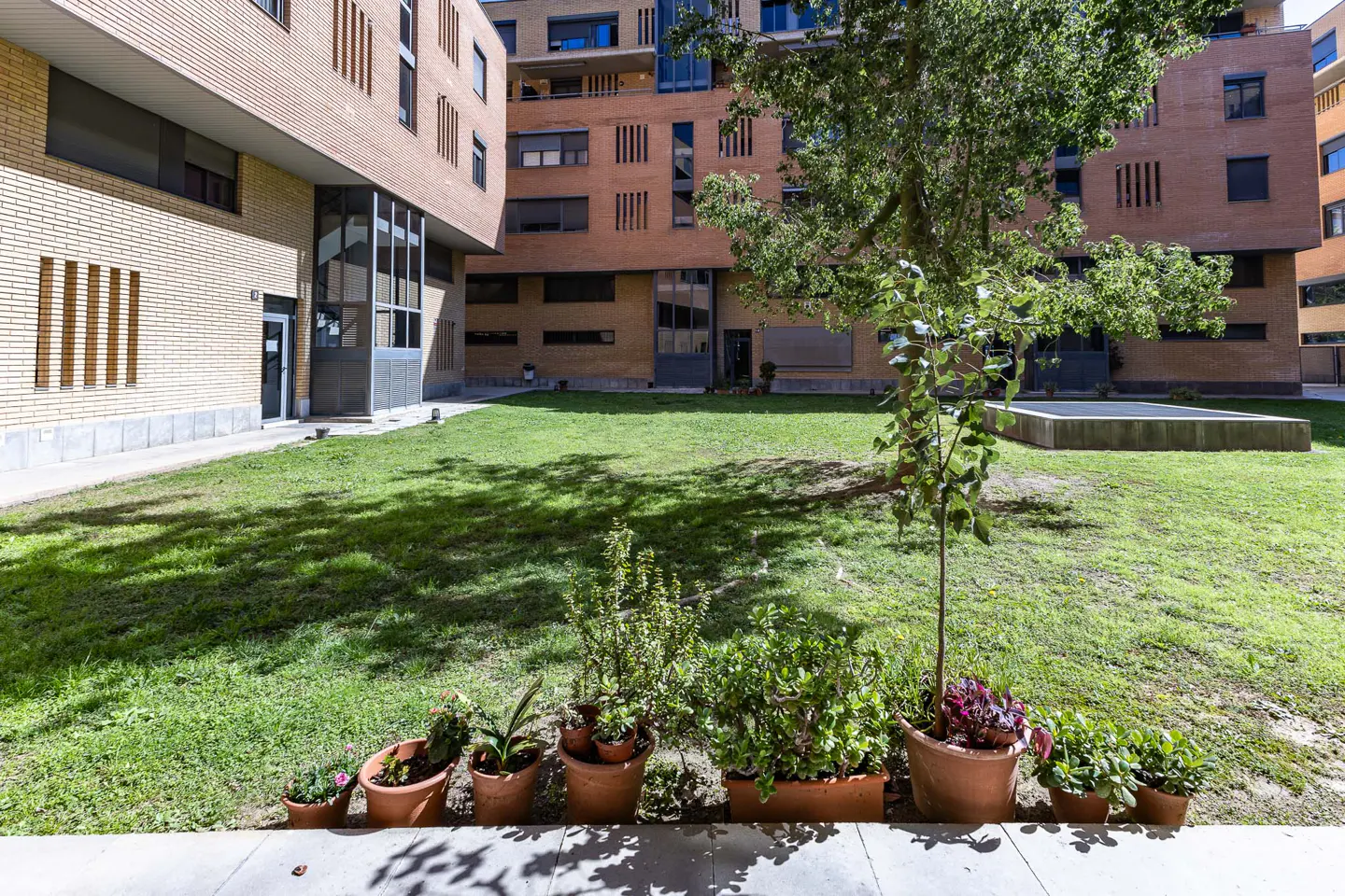 Exterior view of a brick apartment building with a green lawn and potted plants in the foreground.