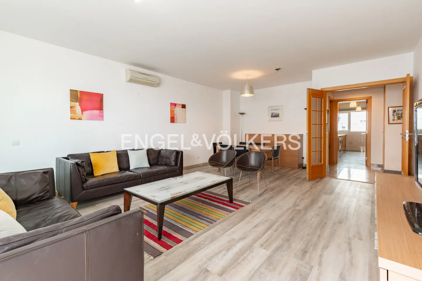 Living room with brown leather sofas, a striped rug, and a dining area with chairs. Light wood floors and white walls.