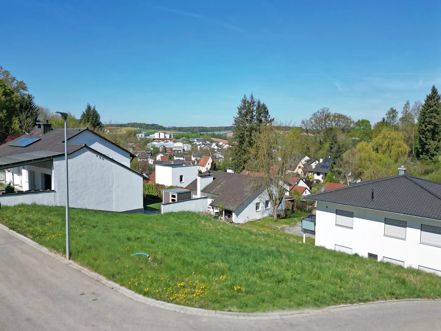 A residential neighborhood with white houses, green lawns, and a clear blue sky.