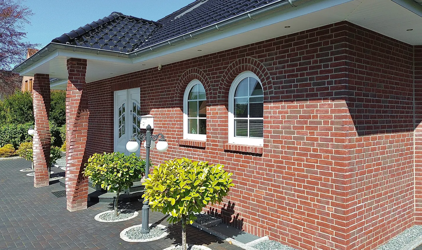 A red brick house with white trim, arched windows, and a black shingled roof. A brick walkway leads to the front door.