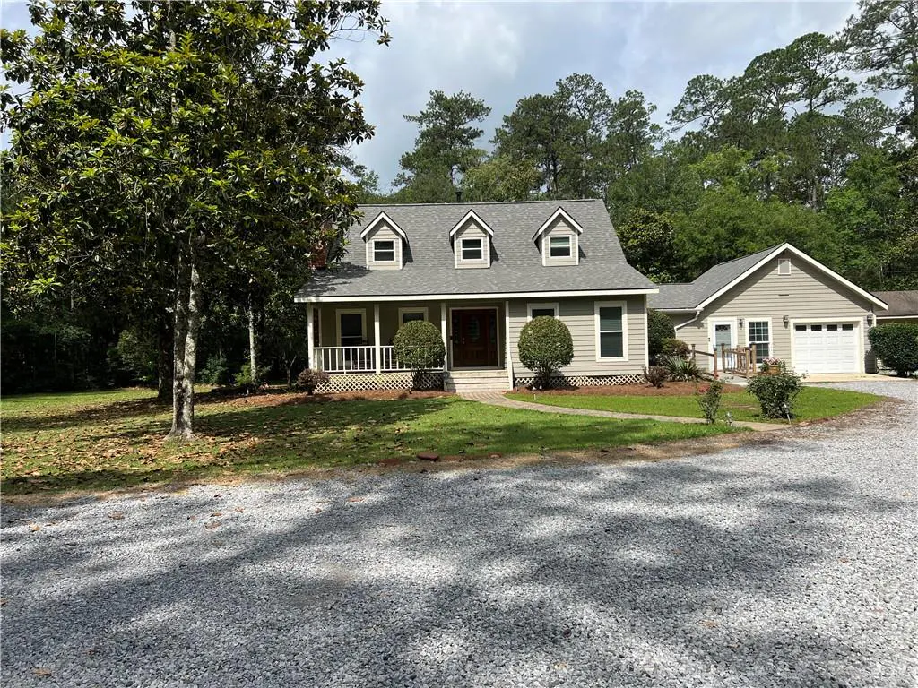 A light-green house with a gray roof and white trim, a front porch, and a gravel driveway.