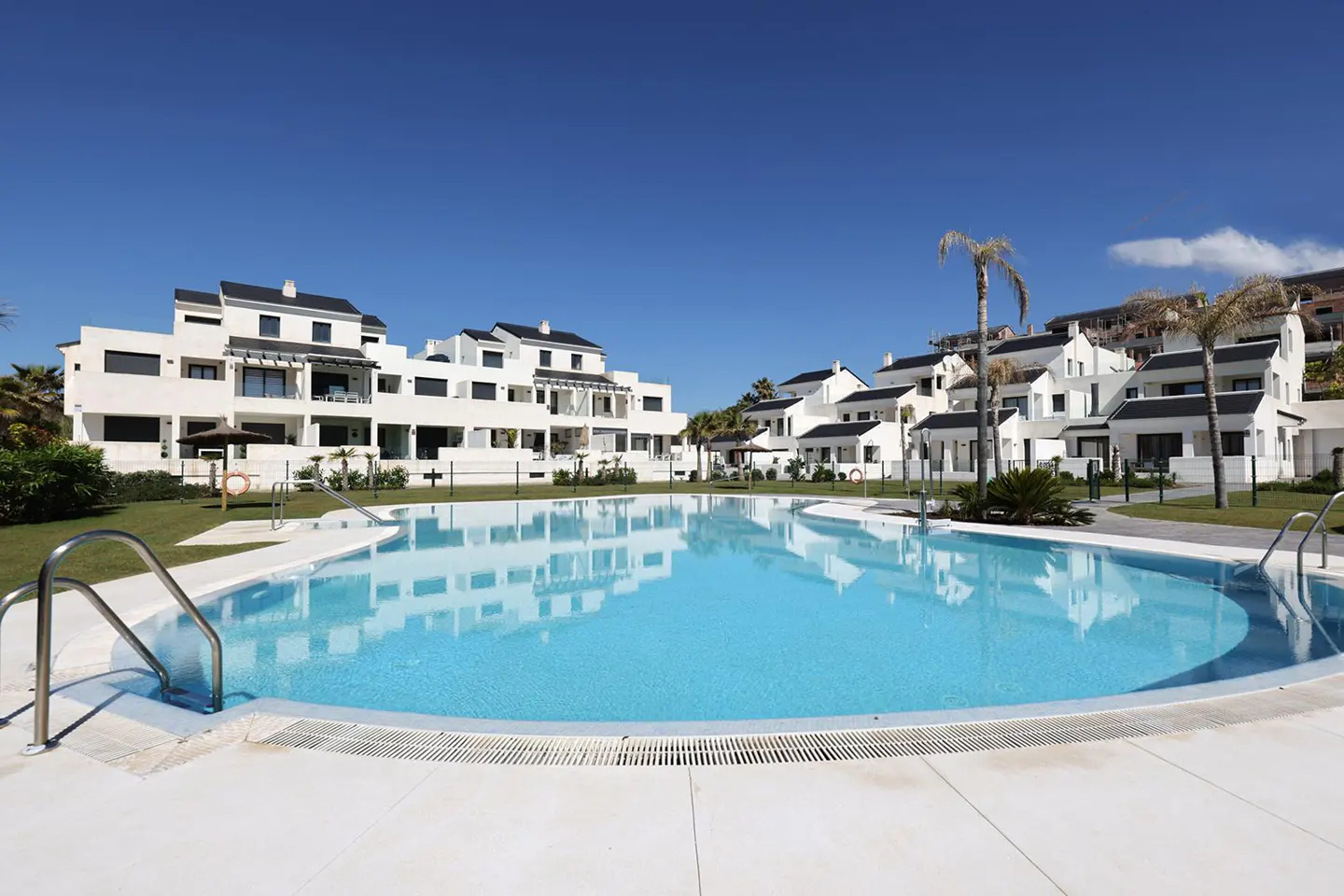 A wide shot of a bright blue pool surrounded by white condos under a clear blue sky.