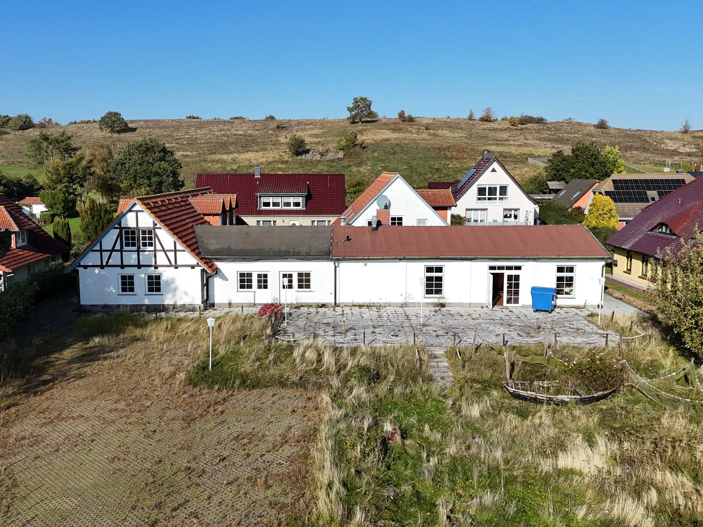 Exterior view of a white house with a red roof, surrounded by a grassy field and other houses.