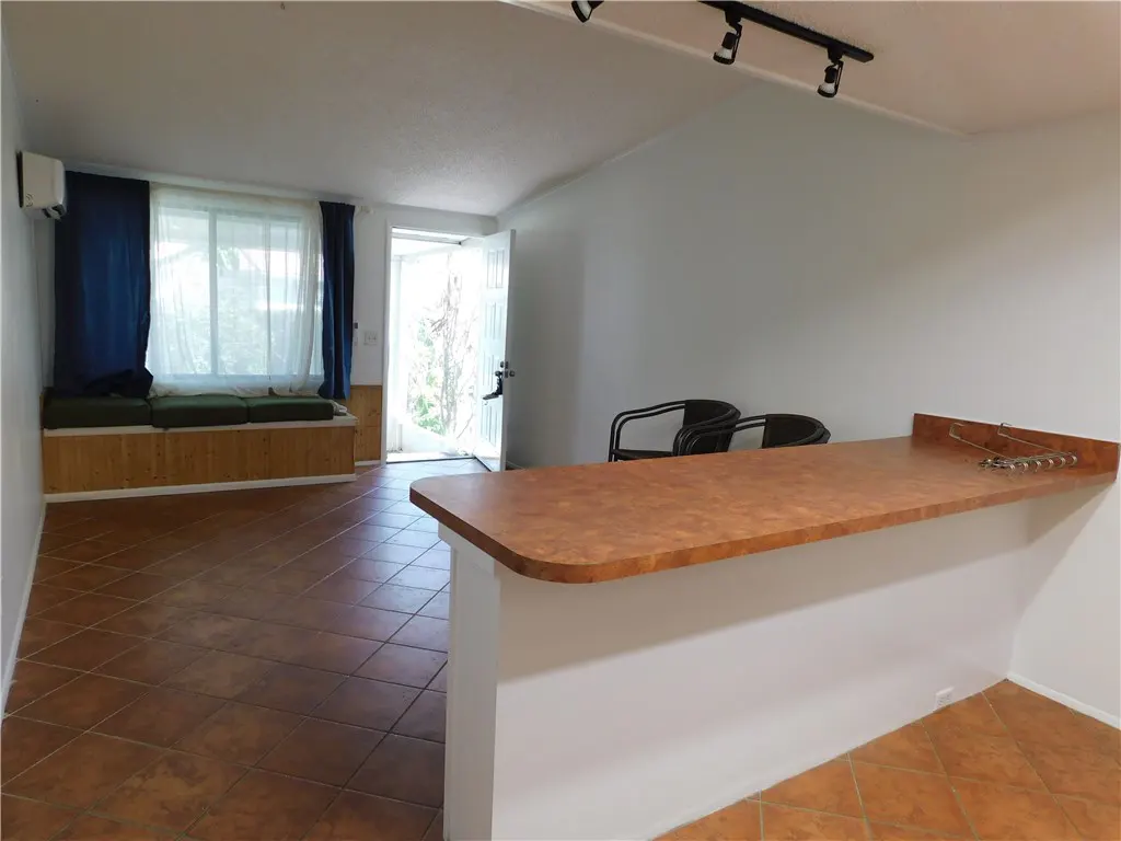 A bright room with brown tile floors, a breakfast bar with two chairs, and a window seat with blue curtains.