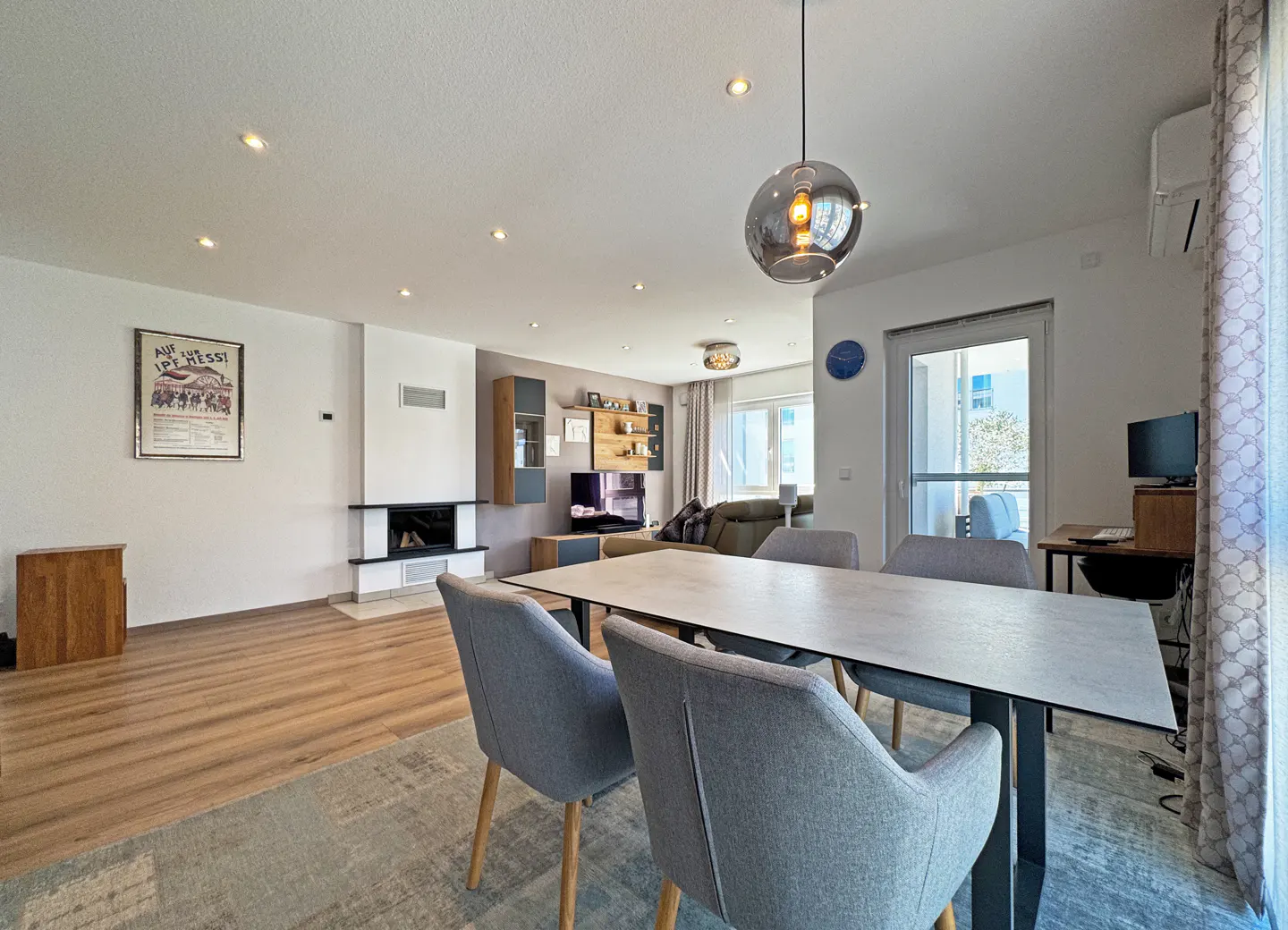 Open-concept living and dining area with wood floors, fireplace, and gray dining set. A glass pendant light hangs above the table.