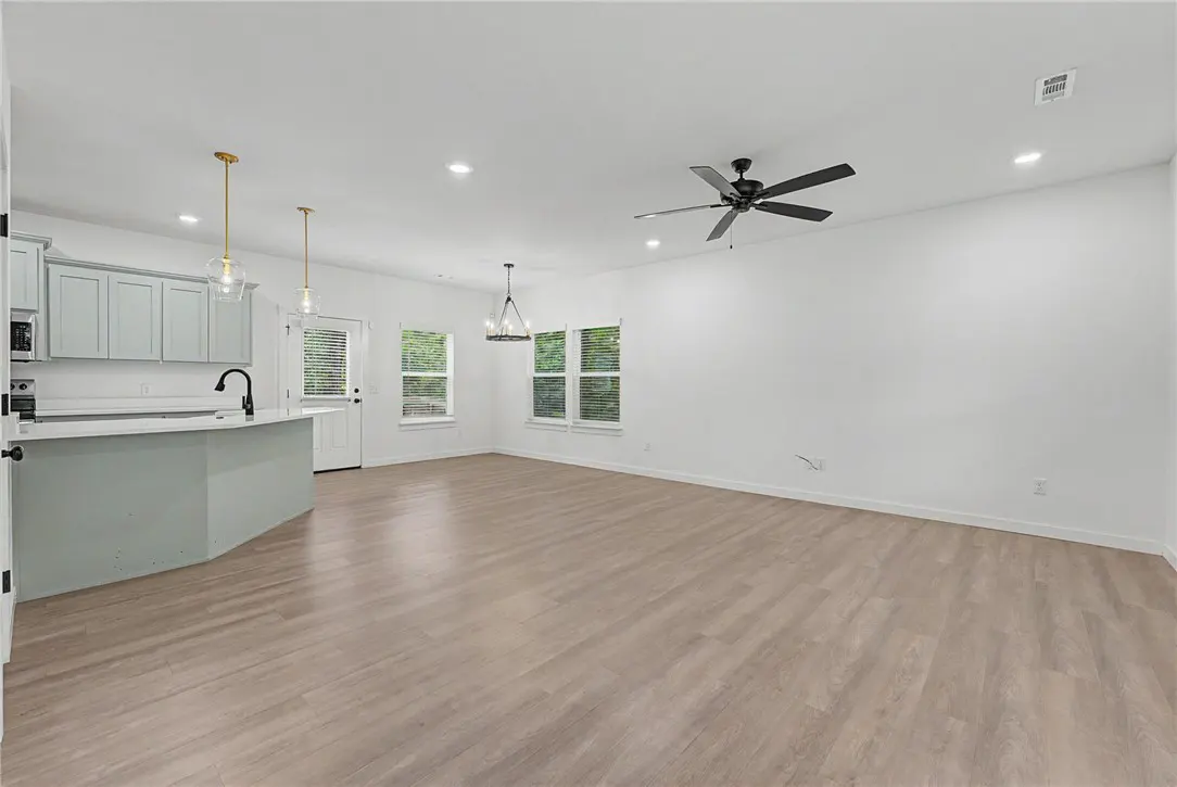 Open-concept living space with light wood floors, white walls, and a kitchen island with light blue cabinets. A black ceiling fan is visible.