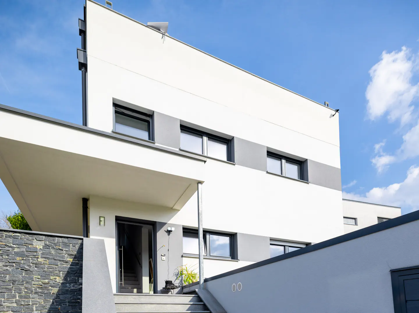 Modern two-story home with white and gray exterior, black-framed windows, and a covered porch. Steps lead to an open front door.