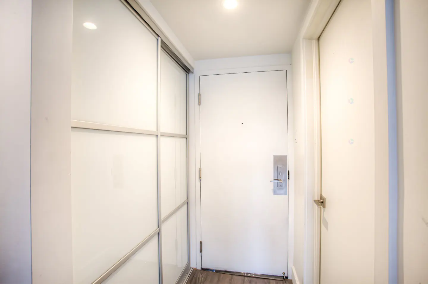 Hallway with white walls, a white door with a silver handle, and a closet with sliding doors.