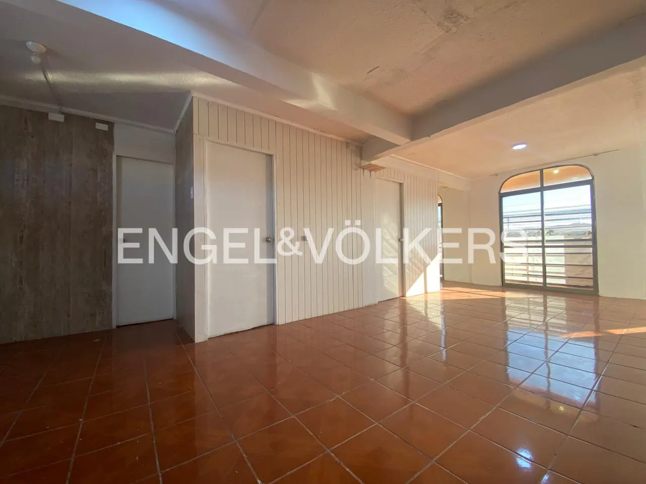 Empty room with brown tile floor, white walls, and a large window with a view. Engel & Völkers logo is visible.