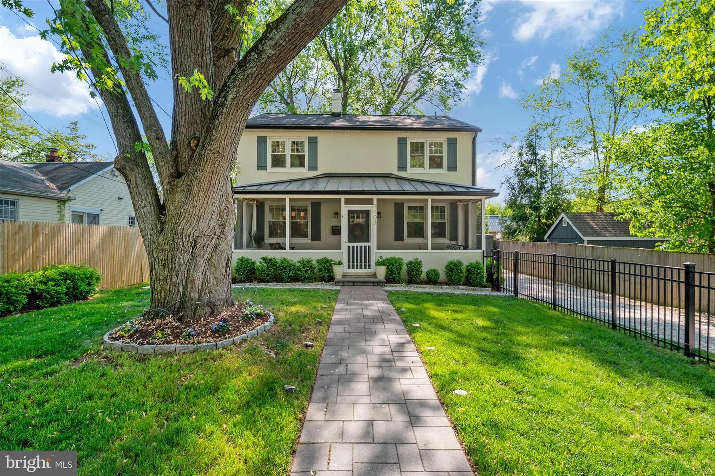 Two-story beige house with blue shutters and a screened-in porch. A brick walkway leads to the front door. A large tree is on the left.