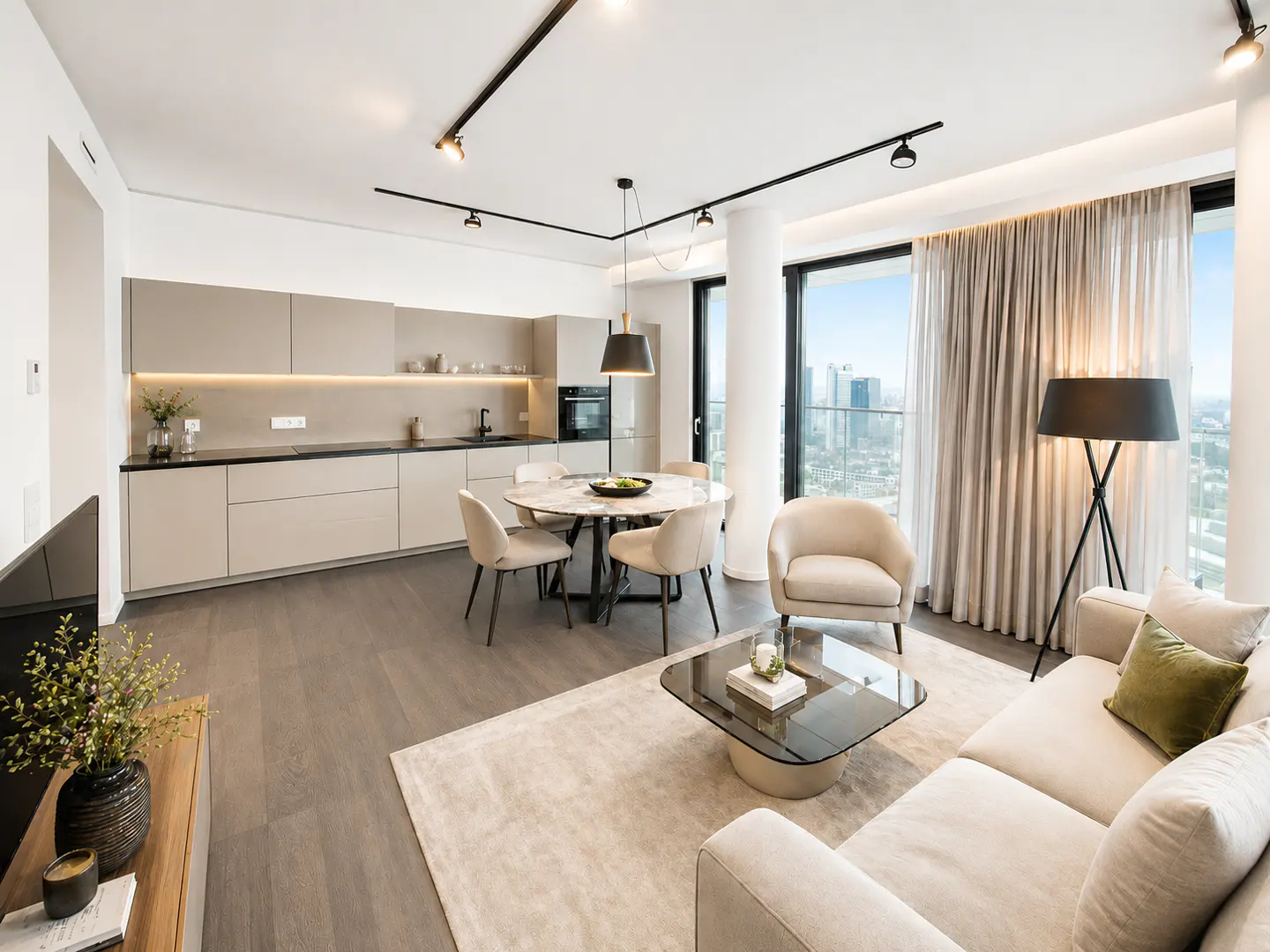 Modern open-plan apartment with a beige kitchen, dining area, and living room featuring floor-to-ceiling city views.