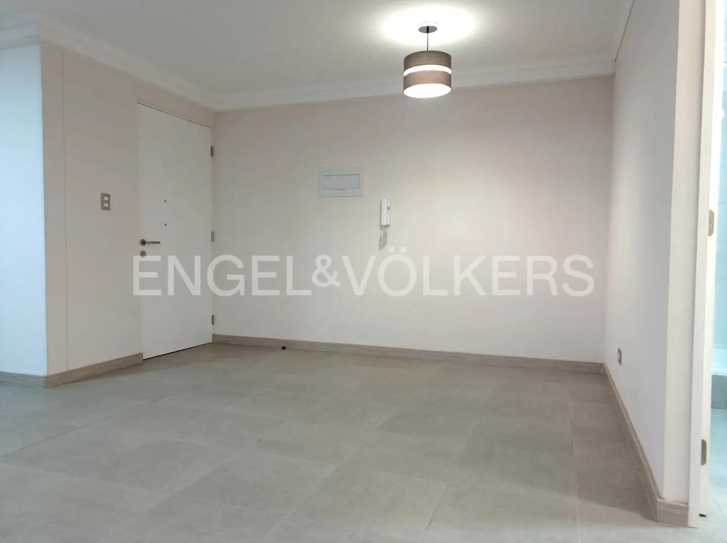 Empty room with light-colored walls, grey tiled flooring, a white door, and a modern pendant light fixture.