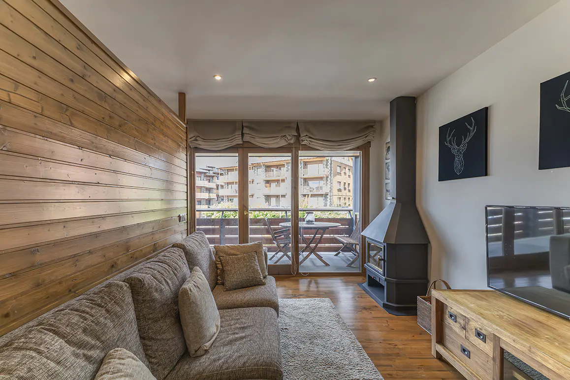 Living room with wood paneled wall, gray sofa, fireplace, and balcony with table and chairs.