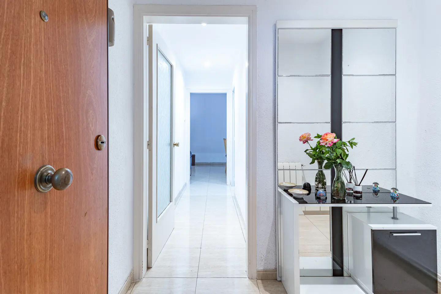 Entryway with a wood door, a long hallway, and a black and white console table with flowers and a mirror.