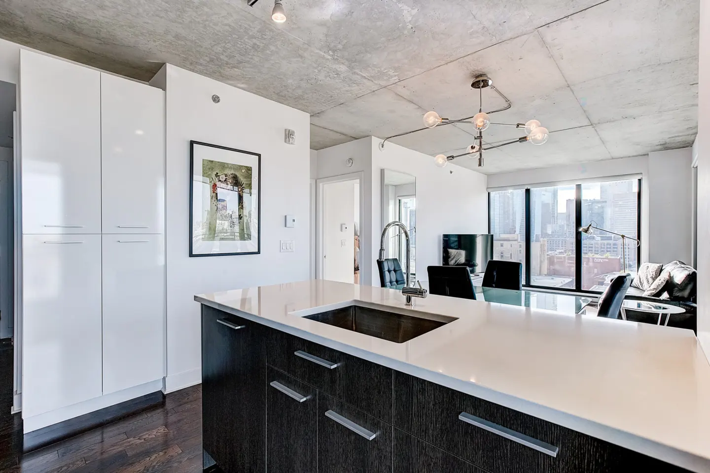A modern kitchen with white cabinets, a dark wood island with a white countertop, and a view of the city skyline.