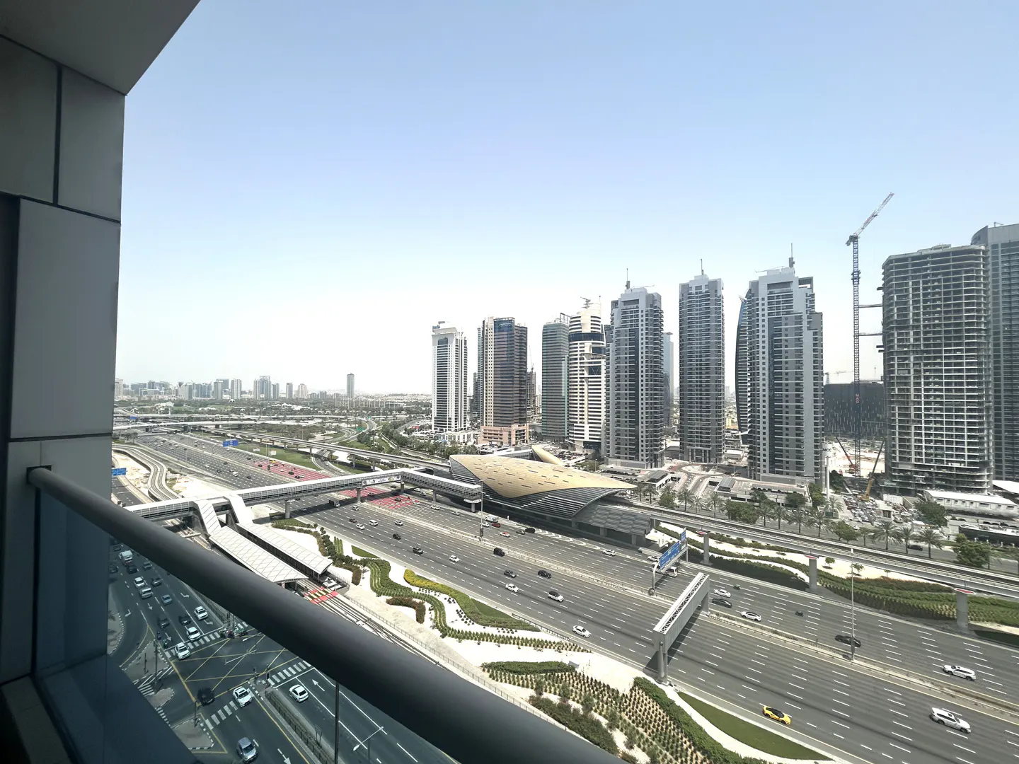 View from a balcony overlooking a busy highway and modern city skyline with tall buildings under a clear blue sky.
